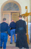 SSPX priest Fr. Michael McMahon being led by the men in blue through the vestibule, down the stairs, to talk things over
with the authorities.  Notice the Crucifix over his right
shoulder... very reminiscent of the Palace Guard,
leading Christ to His death. Will you follow Fr. Michael and take up your Cross as well?